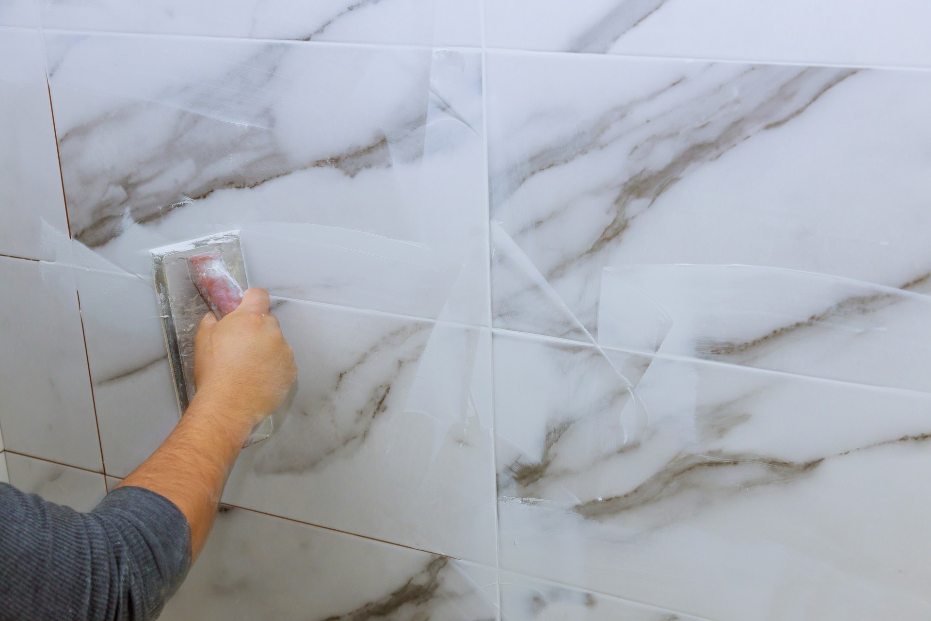 Male hand with the rubber applies grout on a seam between tiles kakelexpress